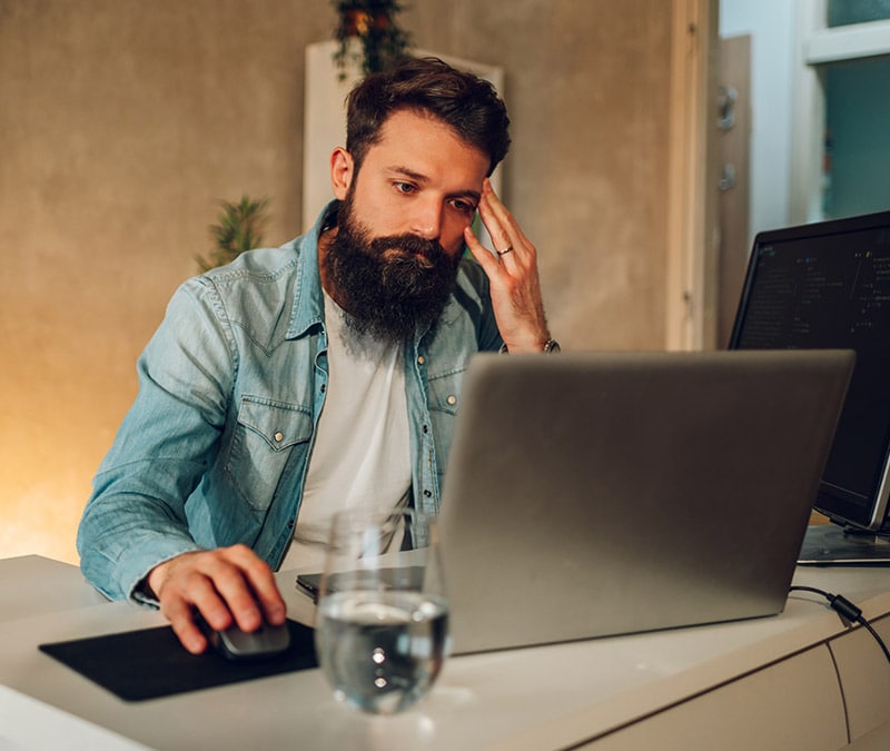 Bearded man researching how to prevent computer viruses on his laptop in a home office setup.