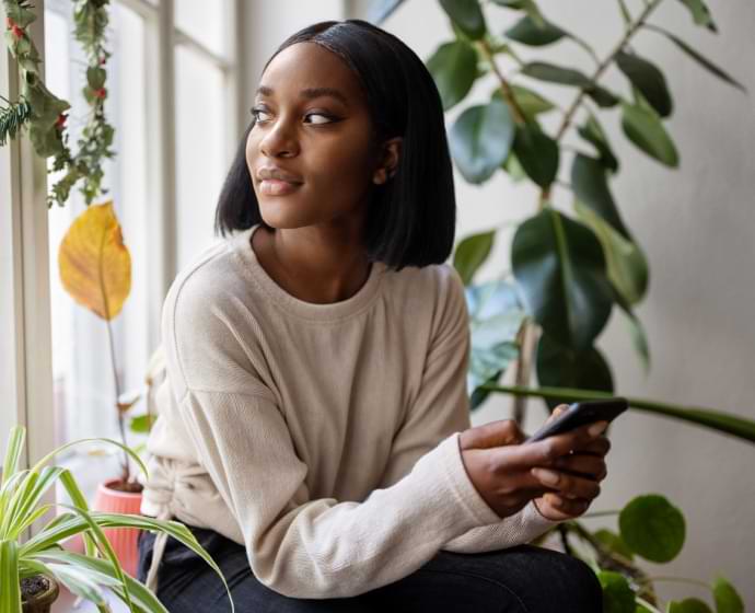 Woman looking out a window while holding a mobile phone